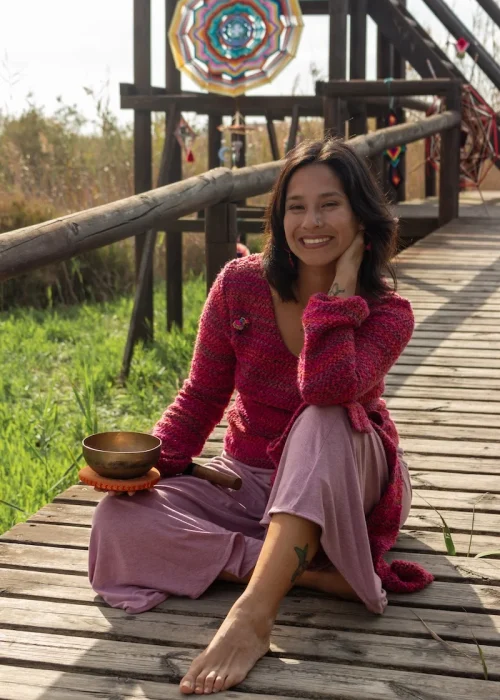 Julia de Entrelanados sentada sobre un camino de madera y un mandala gigante en el fondo